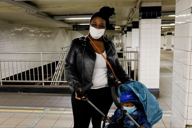 A woman stands in subway station. with mask on, with a stroller with a baby wearing a mask